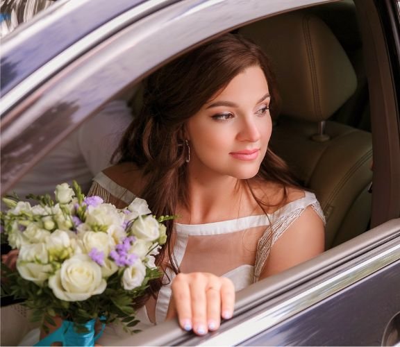 A bride in a white wedding dress , sitting inside a limo