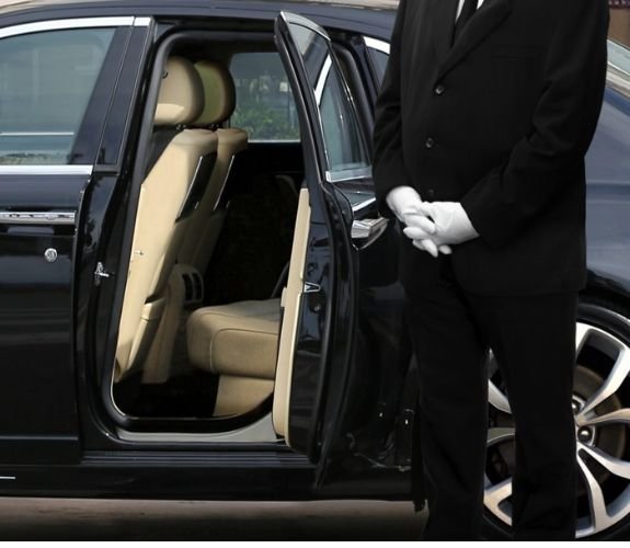 White glove chuaffeur standing next to a black car