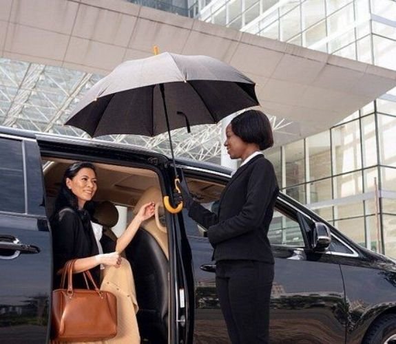 chauffeur assiting a women coming out of a car holding umbrella