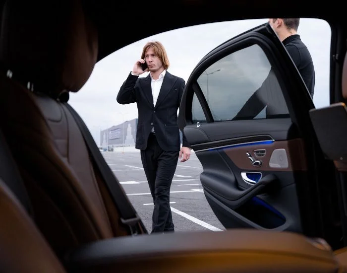 Passenger walking toward chauffeured car while on phone.